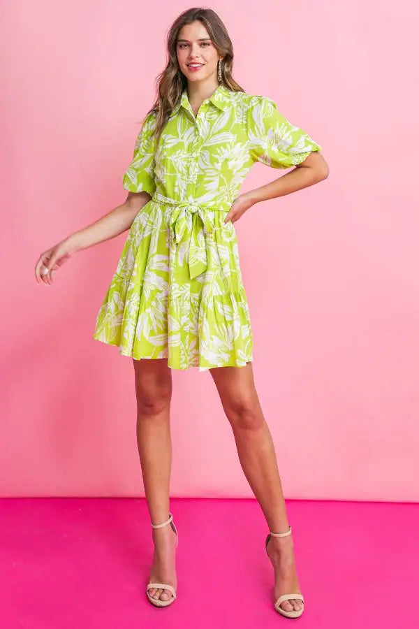 Island time dress. A printed woven mini dress featuring shirt collar, button down, short puff sleeve, self sash tie and ruffled hemline. chartreuse green floral print. 
