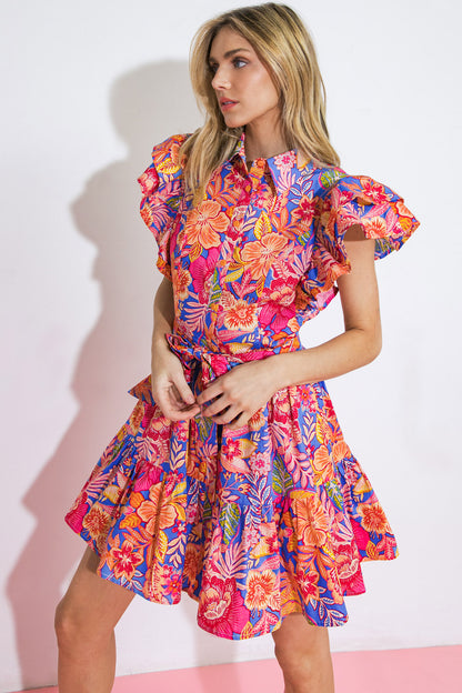 Get ready to add some vacay vibes to your wardrobe with this playful printed mini dress! Featuring a shirt collar, double layered ruffle sleeves, and a ruffled hemline, this dress is perfect for a fun day out. With the added bonus of a self sash tie, you'll have the perfect fit for a carefree yet stylish look.